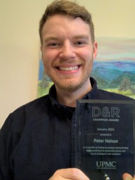 Peter holds his award, smiling.