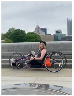 Woman on hand cycle in front of Pittsburgh city skyline.