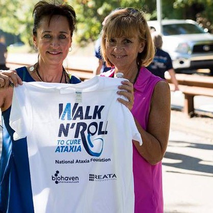 Two women holding up t-shirt, smiling at an outdoor running race.