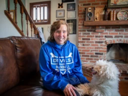 Woman sitting in living room petting white scruffy dog.
