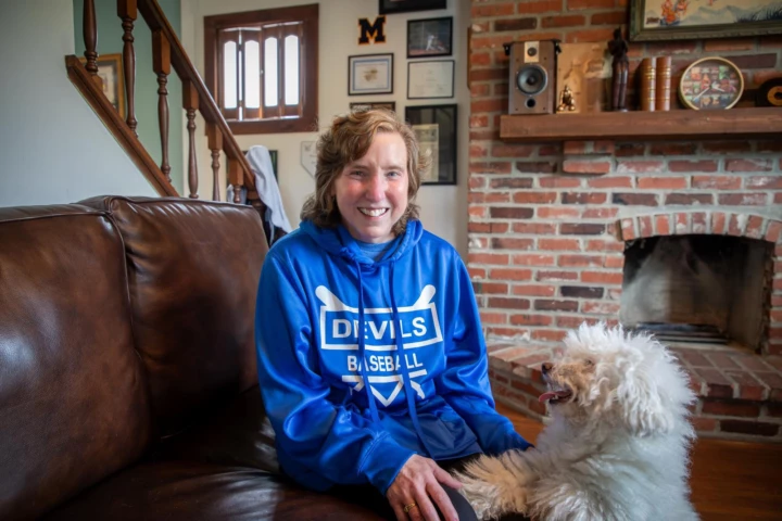 Woman sitting in living room petting white scruffy dog.