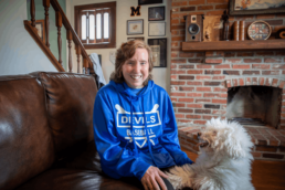Woman sitting in living room petting white scruffy dog.